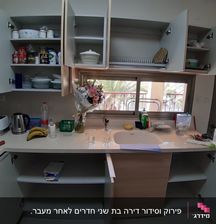 מטבח עם ארונות פתוחים, כלים ומוצרי ניקוי על השיש